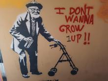 Street art showing an dld man holding a rollator and the text "I don't wanna grow up!!"