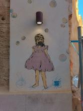 Street art: a girl wearing a face mask below a real lamp